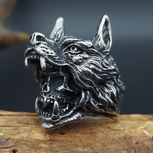 Op de afbeelding: Een zilveren ring met een wolfskop met een gedetailleerd, getextureerd ontwerp. De bek van de wolf is open, waardoor scherpe tanden zichtbaar zijn. De ring is gemaakt van roestvrij staal.
