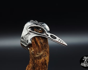 May include: A silver ring with a detailed design of a bird's head with a long beak. The ring is set on a piece of wood.
