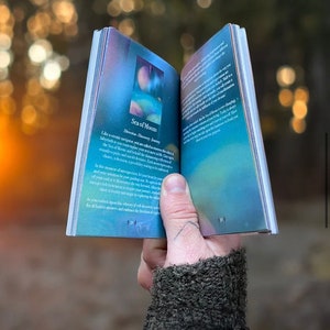 K&ouml;nnte beinhalten: Ein blaues und violettes Buch mit dem Titel "Sea of Moons" und dem Text "Direction: Discovery Journey" auf dem Cover. Das Buch ist auf einer Seite mit einer blauen und violetten Illustration eines Mondes und Sternen ge&ouml;ffnet.