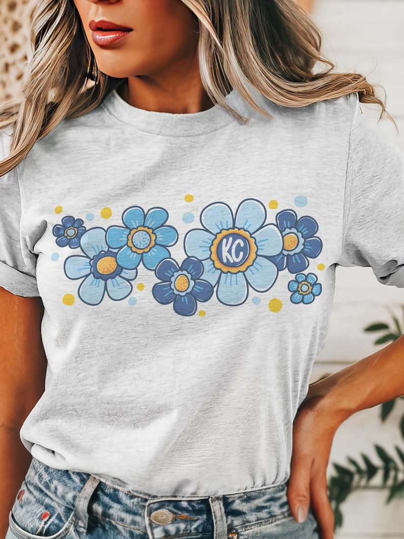 May include: A gray t-shirt with a blue and yellow floral design. The flowers have a yellow center and the letters "KC" are in the center of the largest flower.