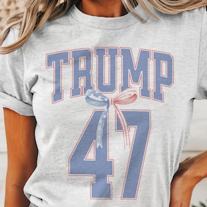 May include: A grey t-shirt with a blue and red design. The design features the text "TRUMP 47" with a red, white, and blue ribbon.