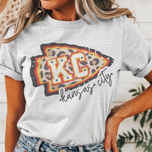 May include: A grey t-shirt with a graphic of a leopard print arrow with the text "KC*kansas*city" in white.
