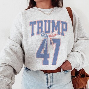 May include: Gray sweatshirt with a blue and red graphic that says "TRUMP 47" with a red, white, and blue ribbon.