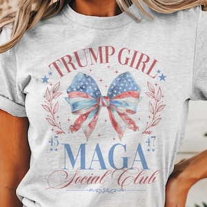 May include: A gray t-shirt with a red, white, and blue bow with stars and the text "TRUMP GIRL" and "Maga Social Club" printed on it.