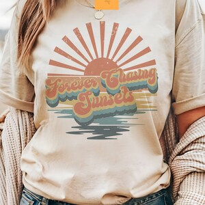 May include: A beige t-shirt with a retro-style graphic of a sunset and the text "Forever Chasing Sunsets".