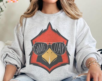 Puede incluir: Sudadera gris con un cardenal rojo que lleva gafas de sol y el texto "GAME DAY".