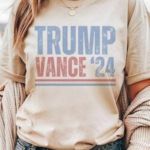 May include: A beige t-shirt with the text "TRUMP VANCE '24" printed in blue and red.