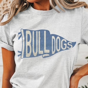May include: A gray t-shirt with a blue and white vintage-style pennant graphic that says "Bulldogs".