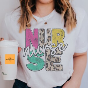 May include: A white t-shirt with a colorful graphic design that says "NURSE" with a leopard print pattern in the middle.