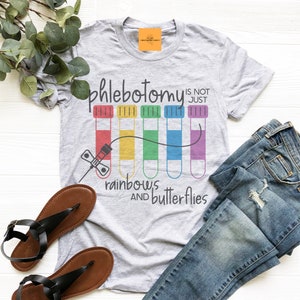 May include: Gray t-shirt with the text "Phlebotomy is not just rainbows and butterflies" and a graphic of a syringe and rainbow colored test tubes.