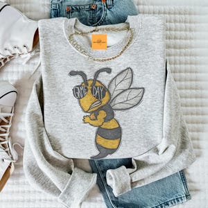 May include: Gray sweatshirt with a cartoon bee wearing sunglasses and the text "Game Day".
