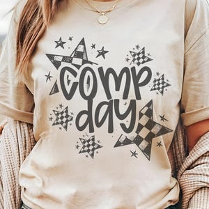 May include: A beige t-shirt with a black and white checkered star design and the text "Camp Day" in black.