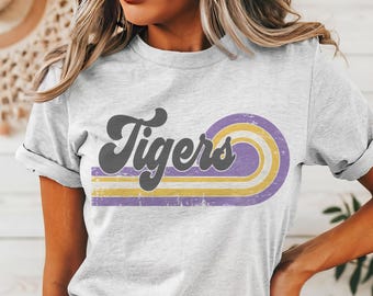 May include: A gray t-shirt with a retro-style graphic that says "Tigers" in black with purple and yellow stripes.