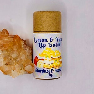 May include: A small cardboard tube with a white label that says "Lemon & Yuzu Lip Balm" and "Stardust & Stems 7g". The label has a colorful illustration of a lemon cake with yellow frosting and lemon slices.
