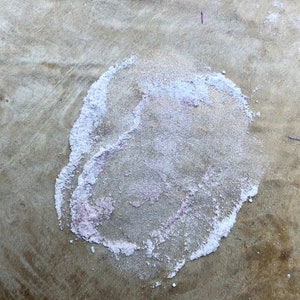 May include: A close-up of a light brown surface with a white and pink circular stain. The stain has a rough, textured surface.