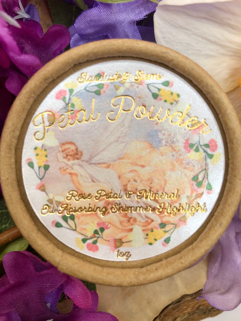 May include: A round, brown container with a white lid featuring a floral design and gold lettering. The lid reads "Stardust & Stems Petal Powder Rose Petal & Mineral Oil Absorbing Shimmer Highlight 10g".