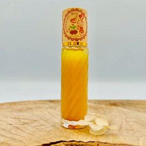 Puede incluir: Una botella de vidrio transparente con un l&iacute;quido amarillo en su interior. La botella tiene una tapa dorada con una fresa de dibujos animados y las palabras "Strawberry Milk" en ella. La botella est&aacute; sobre una superficie de madera con una flor blanca.