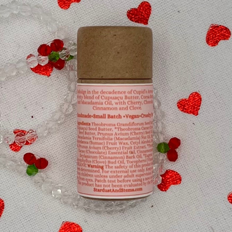 Op de afbeelding: Een bruine kartonnen buis met een roze etiket waarop de ingredi&euml;nten voor een veganistische lippenbalsem staan vermeld. Het etiket bevat de tekst "Cupid's Amorous Blend" en "Small Batch Vegan-Cruelty Free".