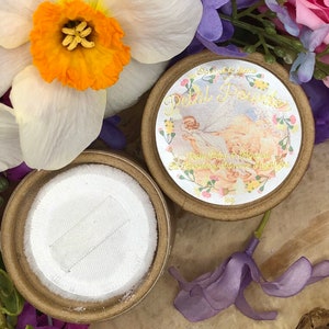 May include: A round, brown container with a white lid. The container has a label that says "Starlight Gems Petal Powder Rose Petal & Mineral  Blending Shine & Light 1oz".