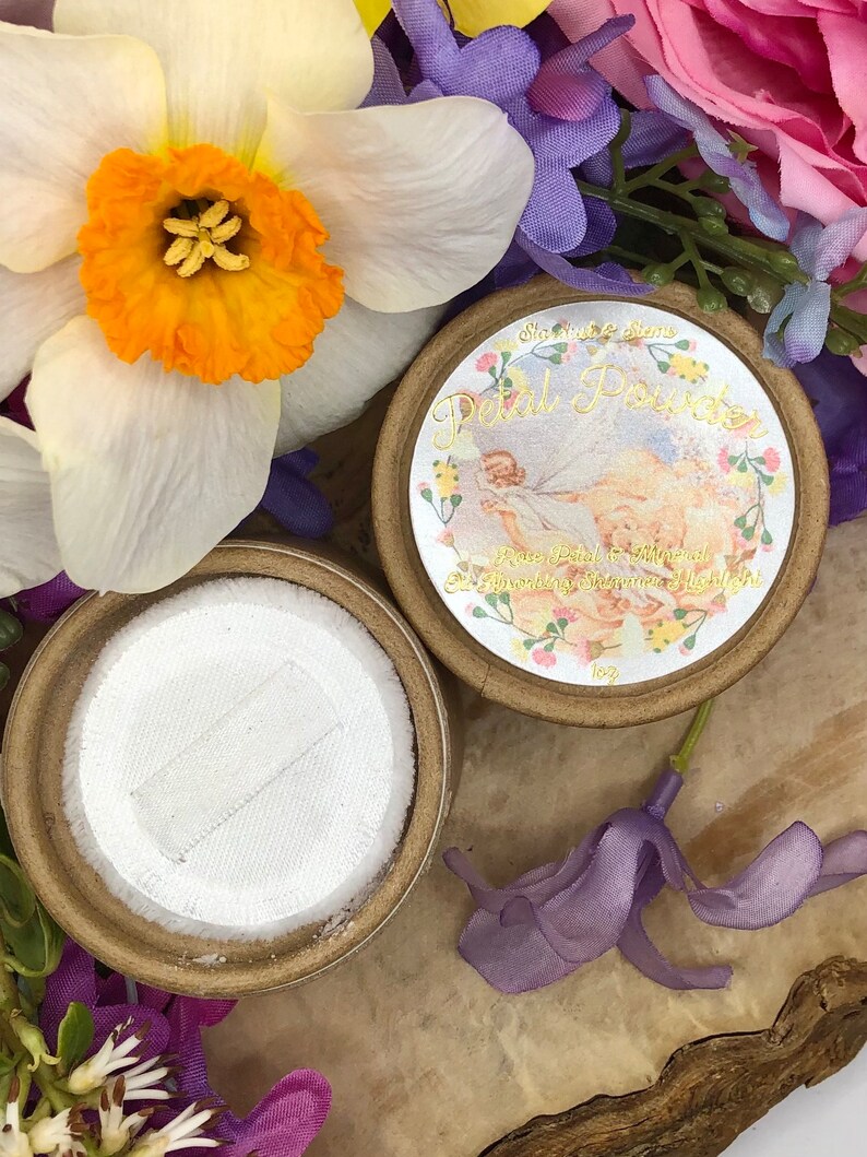 May include: A round, brown container with a white lid. The container has a label that says "Starlight Gems Petal Powder Rose Petal & Mineral  Blending Shine & Light 1oz".