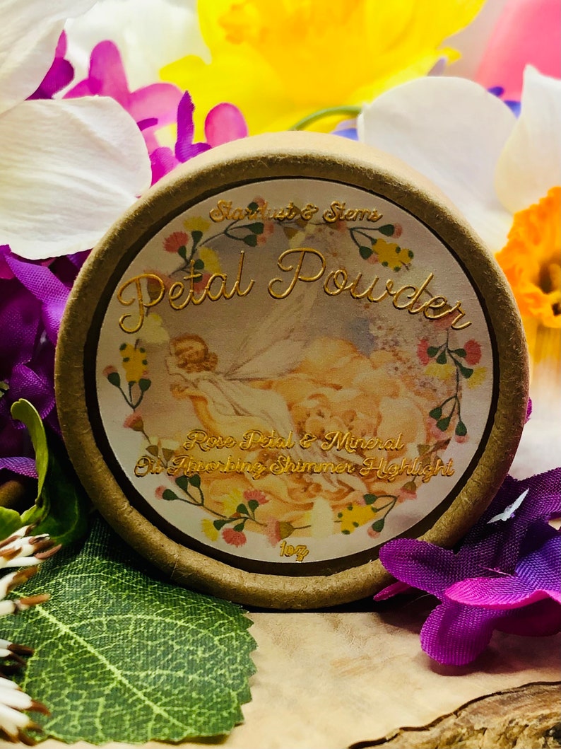 May include: A round, brown container with a gold lid and label. The label features a floral design and the text "Starlight & Stems Petal Powder Rose Petal & Mineral Shimmer Highlight 1 oz".