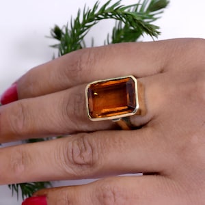 May include: A gold ring featuring a large, rectangular, amber-colored gemstone. The ring has a simple, elegant design with a gold band. The gemstone is the focal point, showcasing its warm, rich color. The ring is a statement piece, perfect for adding a touch of luxury.