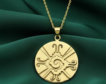 May include: Gold-colored pendant necklace featuring a circular pendant with an intricate design. The pendant has a central spiral and radiating lines, with decorative elements around the edge. The necklace hangs on a delicate gold chain, set against a dark green background.