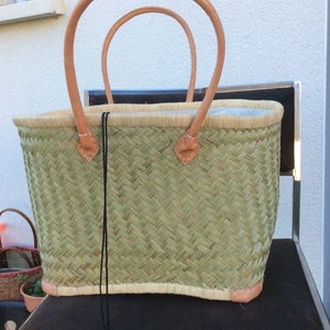 May include: A woven green basket with leather handles. The basket has a light brown trim and a black drawstring.