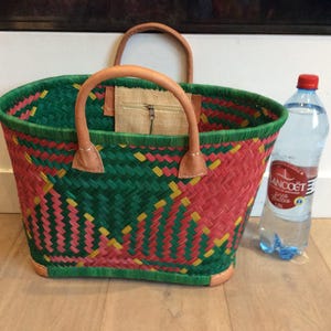 May include: A woven tote bag with a green, pink, and yellow pattern. The bag has leather handles and a zippered pocket on the inside.