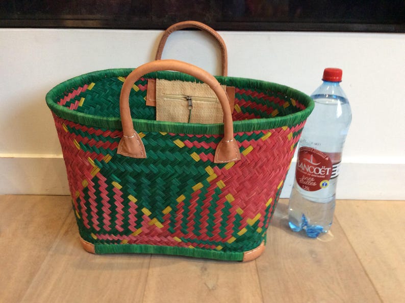 May include: A woven tote bag with a green, pink, and yellow pattern. The bag has leather handles and a zippered pocket on the inside.