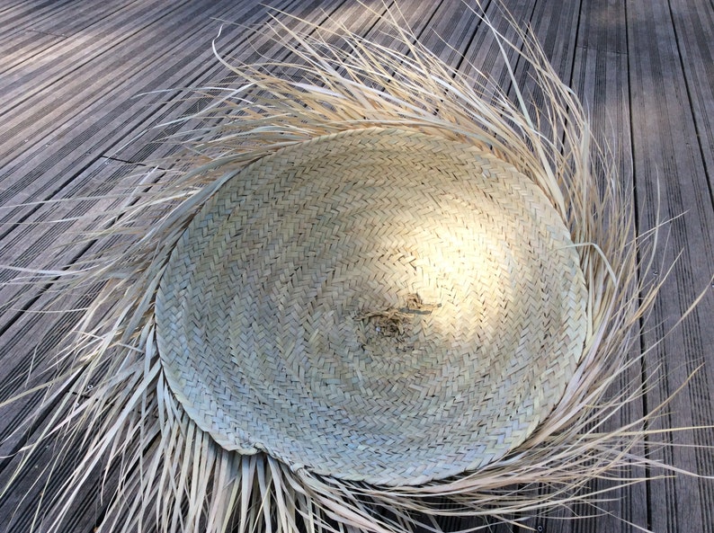 Op de afbeelding: Een grote, ronde, geweven strohoed met een brede rand en een natuurlijke, lichtbruine kleur. De hoed is gemaakt van strak geweven stro en heeft een licht getextureerd oppervlak.