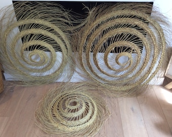 Peut inclure: Trois décorations murales tissées en matériaux naturels, chacune avec un motif en spirale. Les pièces sont circulaires et de couleur brun clair.