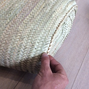 May include: Close-up of the woven edge of a natural straw tote bag. The bag is made of a tightly woven, light brown material.