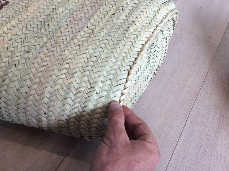 May include: Close-up of the woven edge of a natural straw tote bag. The bag is made of a tightly woven, light brown material.