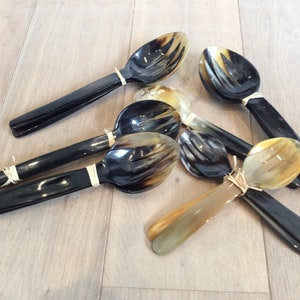 Può includere: Un set di sei cucchiai e forchette in corno. I cucchiai e le forchette sono in corno marrone scuro e marrone chiaro. I manici sono legati insieme con lo spago.