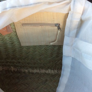 May include: A woven straw tote bag with a white cotton lining and a zippered pocket. The bag has a natural straw colour and a green woven pattern.