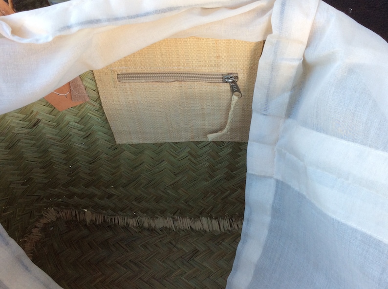 May include: A woven straw tote bag with a white cotton lining and a zippered pocket. The bag has a natural straw colour and a green woven pattern.