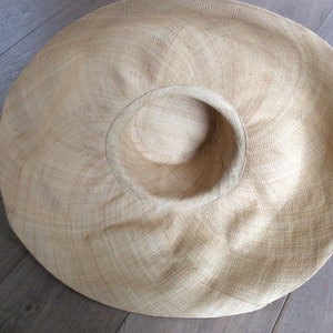 Puede incluir: Un sombrero de paja grande y de ala ancha de color marr&oacute;n claro. El sombrero est&aacute; hecho de paja tejida y tiene una corona grande y redonda.