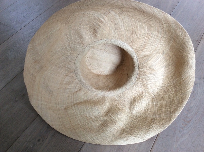 Puede incluir: Un sombrero de paja grande y de ala ancha de color marr&oacute;n claro. El sombrero est&aacute; hecho de paja tejida y tiene una corona grande y redonda.