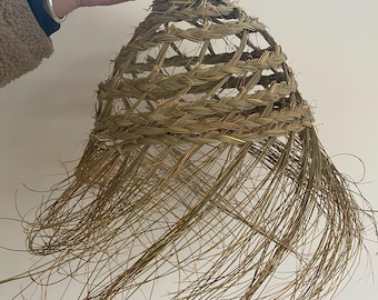 May include: A woven lampshade made of natural materials, with a long, flowing fringe. The lampshade is light brown in color and has a rustic, handmade look.