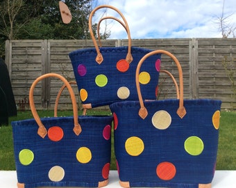 May include: Three blue woven tote bags with colourful polka dots. Each bag has tan leather handles and accents. The bags are different sizes, with the largest at the back and the smallest at the front.