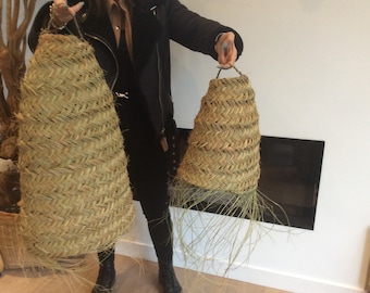 May include: Two natural woven pendant light shades with fringe details. The shades are made of a natural material, possibly straw or seagrass, and have a woven pattern. The shades are hanging from a white ceiling.