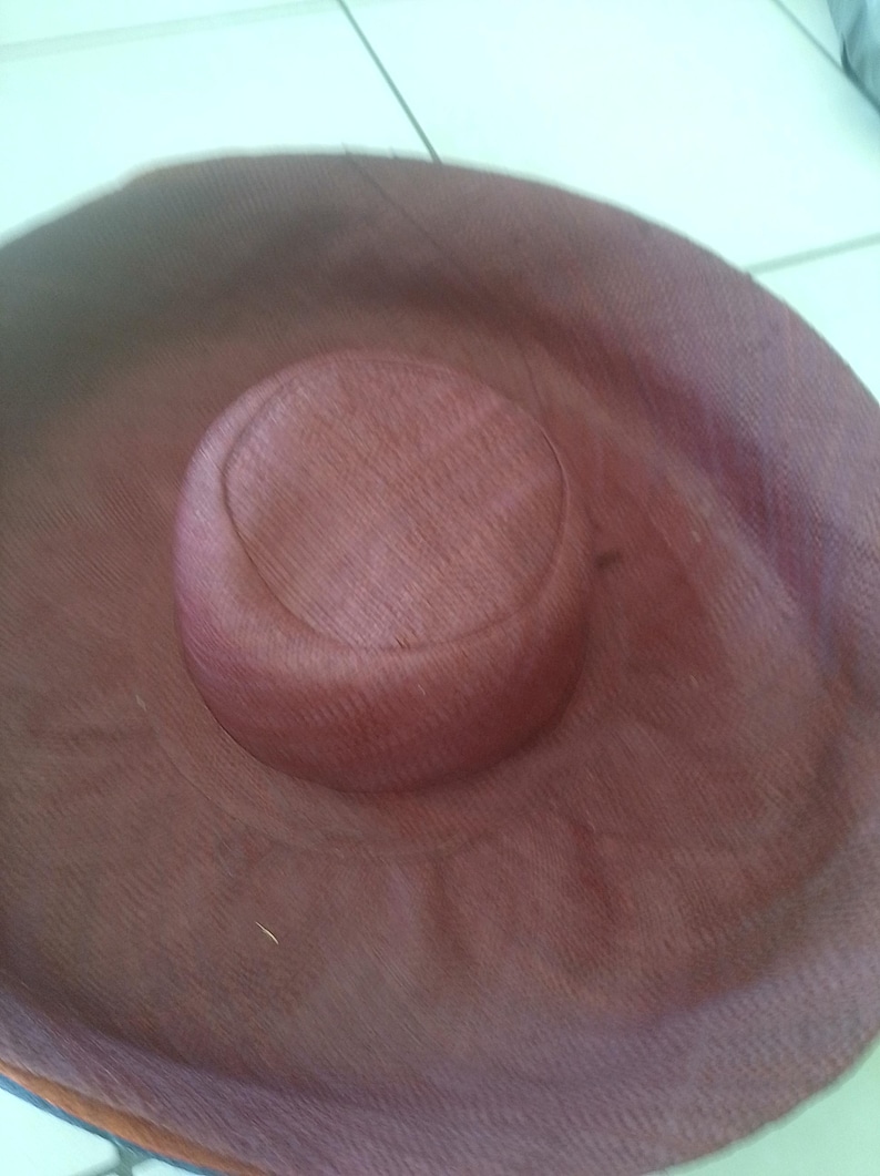 Puede incluir: Un sombrero grande, redondo y marr&oacute;n hecho de material tejido. El sombrero tiene un ala ancha y una corona poco profunda.