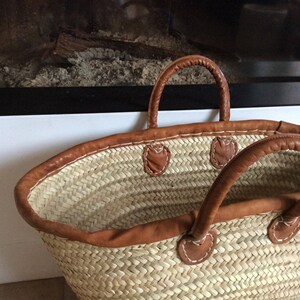 May include: A large, woven straw tote bag with brown leather handles and trim. The bag has a wide, open top and is perfect for carrying groceries or other items.