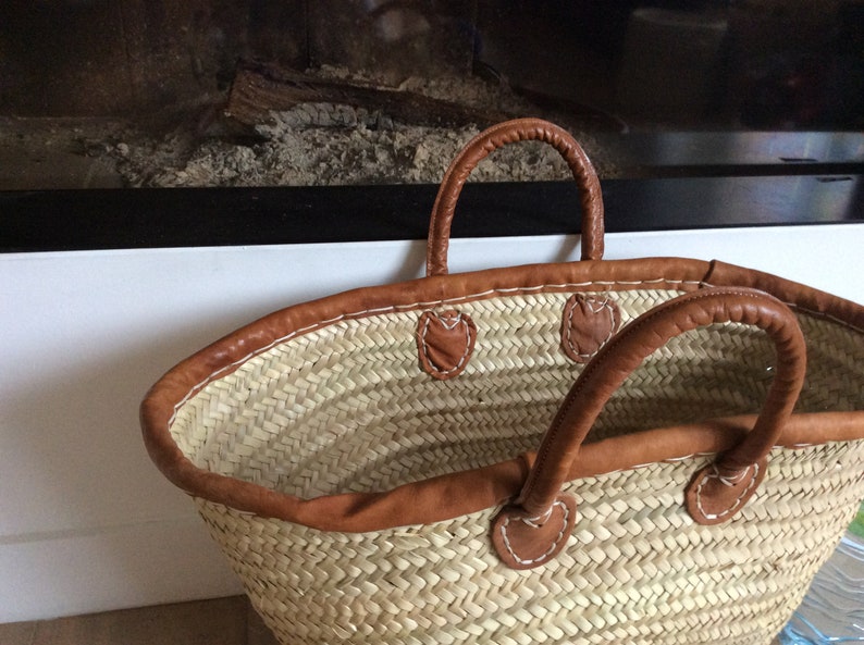 May include: A large, woven straw tote bag with brown leather handles and trim. The bag has a wide, open top and is perfect for carrying groceries or other items.