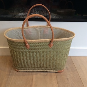 May include: A green woven basket with leather handles. The basket is empty and has a white lining.