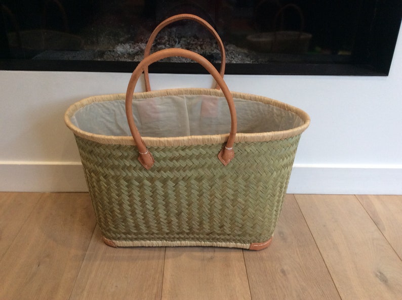 May include: A green woven basket with leather handles. The basket is empty and has a white lining.