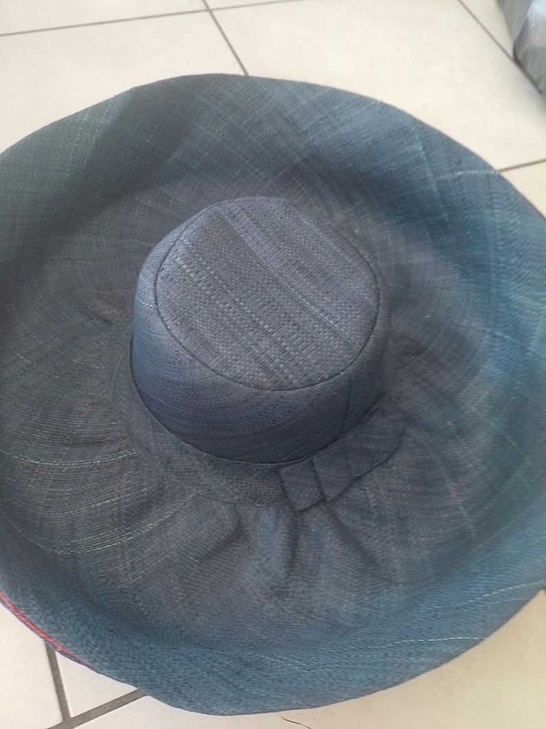Puede incluir: Un sombrero de sol grande y de ala ancha hecho de paja tejida. El sombrero es de color azul oscuro y tiene una corona ligeramente redondeada.