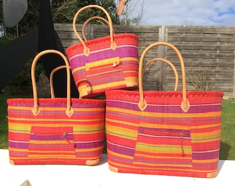 May include: Three colorful striped woven tote bags with leather handles. The bags are stacked on top of each other. The bags have a small zippered pocket on the front.