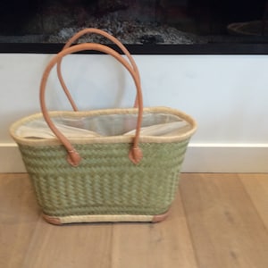 May include: A green woven tote bag with leather handles. The bag is empty and has a white lining.